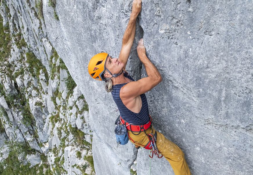 Kletterer an einer steilen Felswand, ausgestattet mit Helm und Klettergurt.