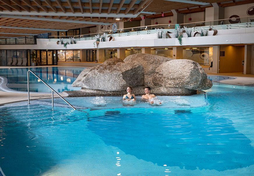 Innenpool mit zwei Personen und einer Felseninsel in der Mitte.