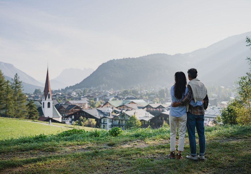 Paar genießt den Ausblick auf die malerische Region Seefeld mit einer Kirche im Vordergrund und Bergen im Hintergrund.