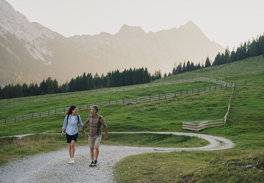 Paar wandert auf einem Pfad durch grüne Wiesen, Berge im Hintergrund. Ideal für Wandern in der Region Seefeld.