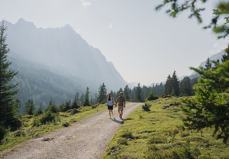 Ein Paar wandert auf einem Weg durch eine grüne Berglandschaft.