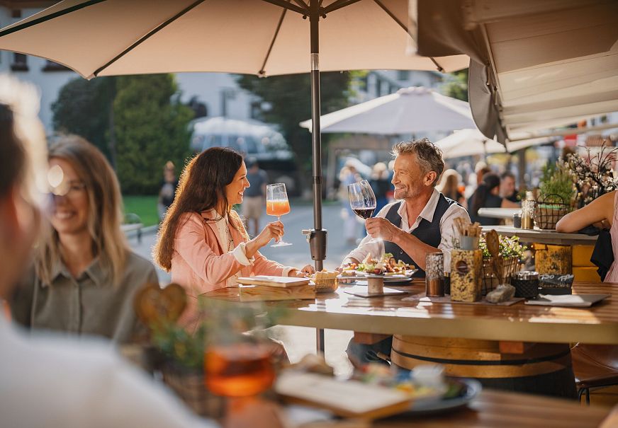 Zwei Personen in einem Freiluftrestaurant stoßen mit Getränken an.