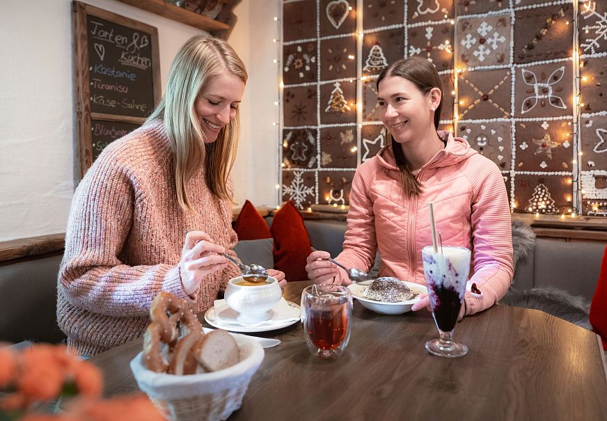 Zwei Frauen sitzen in einem Café und genießen Desserts und Getränke.