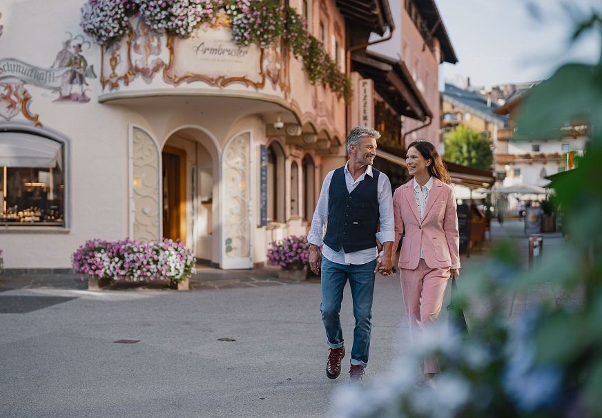 Paar spaziert durch malerische, blumengeschmückte Straße in der Region Seefeld.