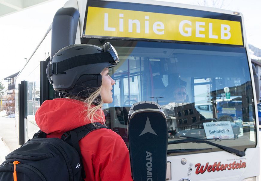 Eine Frau in Skikleidung steht vor einem Bus mit der Aufschrift 'Linie GELB'.