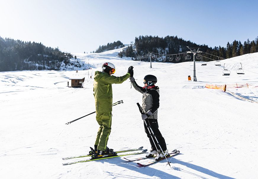 Zwei Skifahrer auf einer schneebedeckten Piste, die einander feiern.