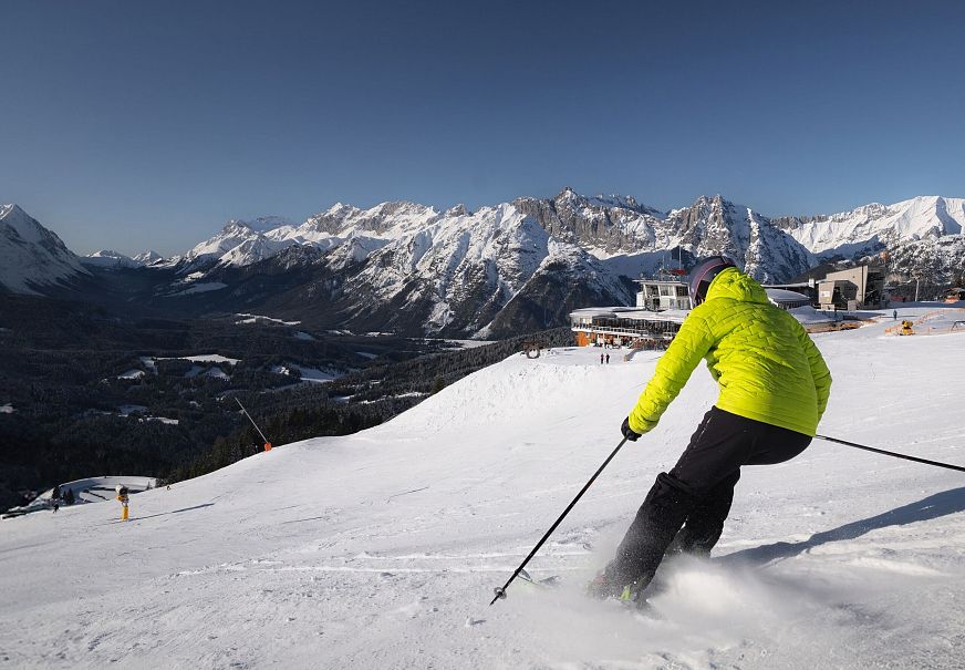 Skifahrer in gelber Jacke auf Piste in der Region Seefeld, umgeben von schneebedeckten Bergen.