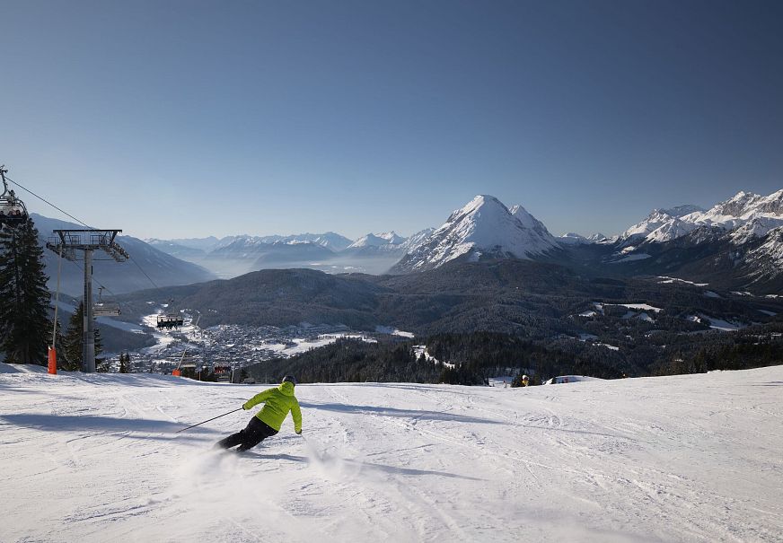 Skifahrer auf Piste in der Region Seefeld, umgeben von verschneiten Bergen und klarem Himmel.