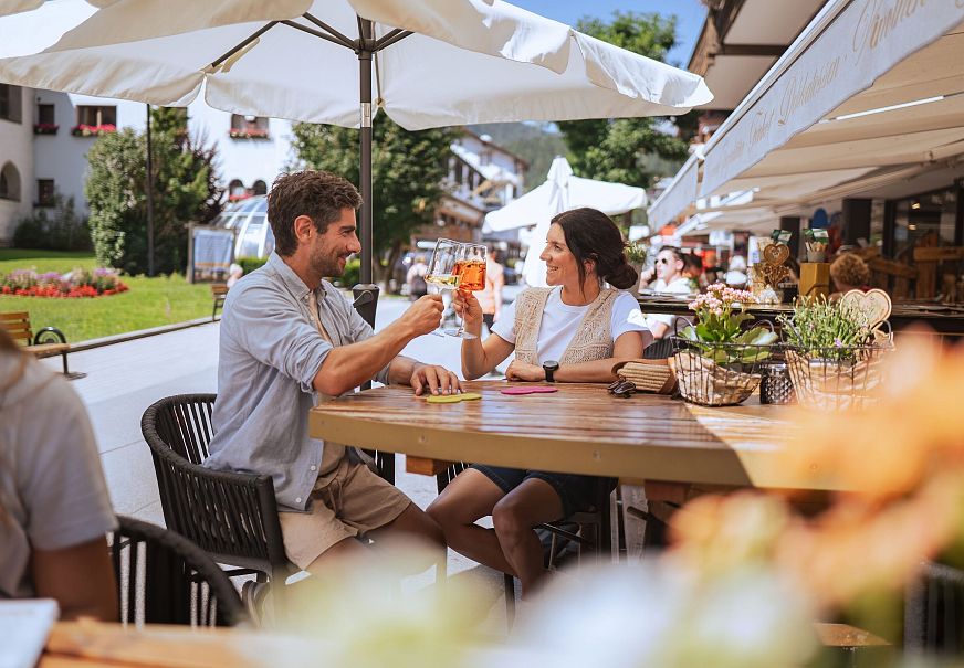 A couple toasting drinks at an outdoor café on a sunny day.