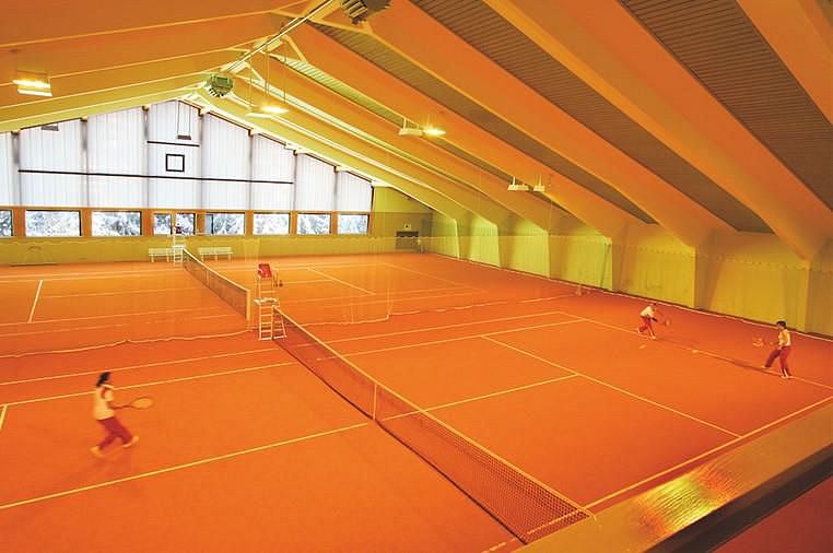Zwei Tennisspieler spielen in einer hellen Halle auf einem orangenen Platz.