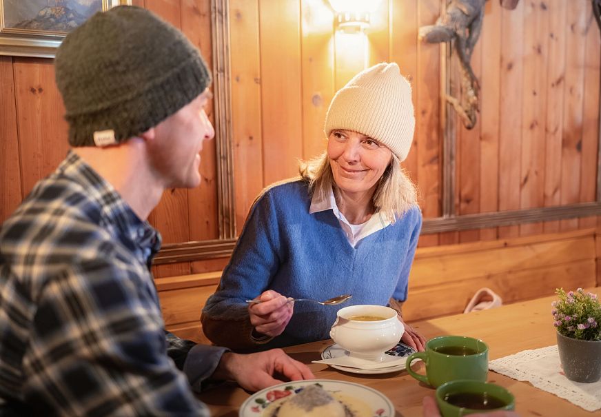 Winterwandern im Wildmoos_Paar kehrt ein in der Lottenseehütte_Frau lächelt Mann an