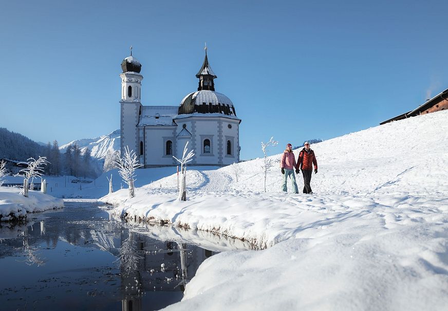 Winterwandern in der Region Seefeld_Mann und Frau laufen vor dem Seekirchl_Weitwinkel