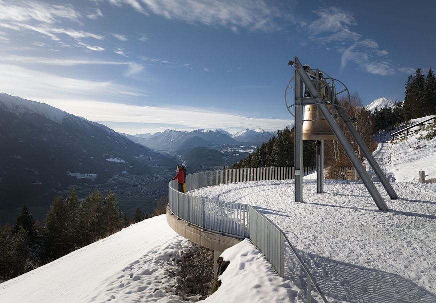 Person in roter Kleidung auf Aussichtsplattform mit Blick auf schneebedeckte Berge.