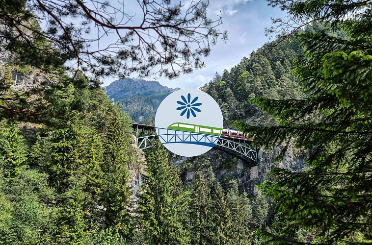 Eine Brücke mit einem roten Zug, umgeben von grünen Bäumen und Bergen.