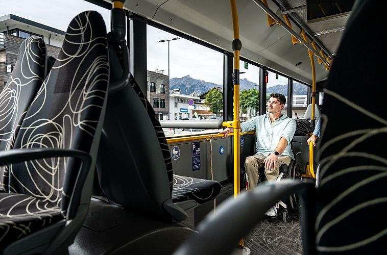 Mann im Stadtbus schaut aus dem Fenster, Berge und Gebäude im Hintergrund sichtbar.