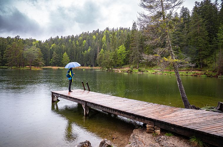 Eine Person auf einem Holzsteg am See mit einem Regenschirm.