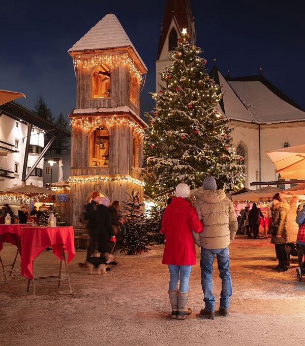 Weihnachtsmarkt mit festlichen Ständen, großer Tanne und Besuchern in winterlicher Atmosphäre.