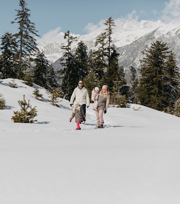 Paar beim Winterwandern in einer schneebedeckten Landschaft mit Bäumen und Bergen.