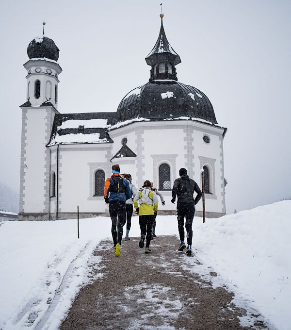 Läufergruppe vor verschneiter Kirche mit Zwiebelturm, Winterlauf in der Region Seefeld.