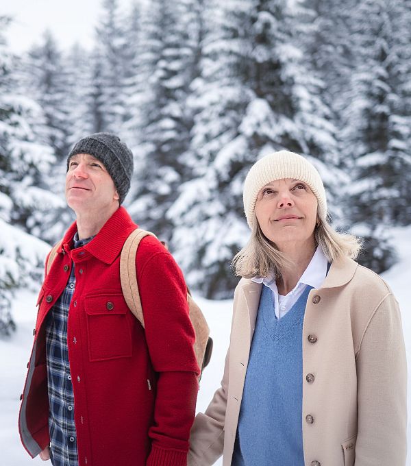 Winterwandern im Wildmoos_Paar läuft durch verschneiten Wald_Frau blickt in die Bäume