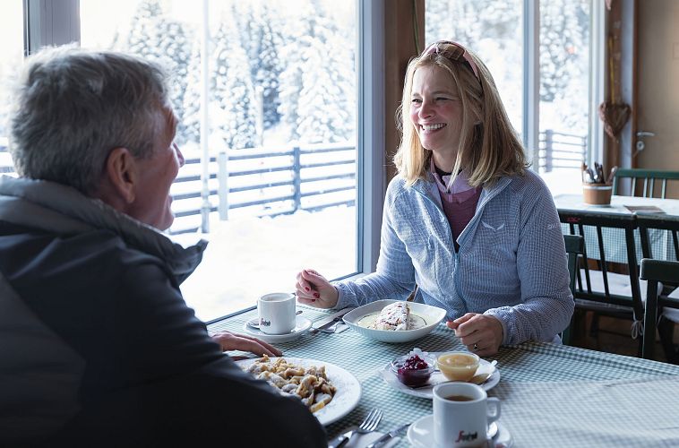 A woman smiling at a man in a cozy cafe with snowy scenery outside.