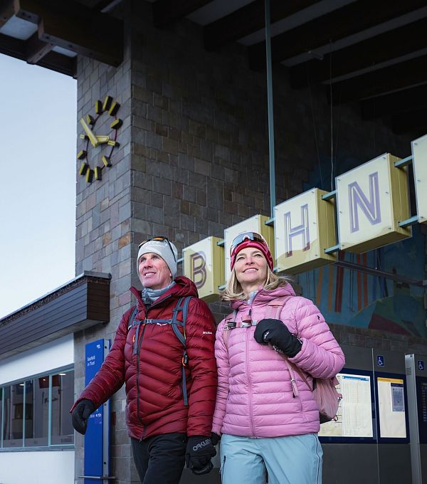 Winterwandern in der Region Seefeld_Mann und Frau kommen in Seefeld aus dem Bahnhof_Nahaufnahme