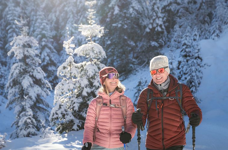 Winterwandern in der Region Seefeld_Mann und Frau wandern im Fludertal durch den Wald_Nahaufnahme Mann und Frau lächeln