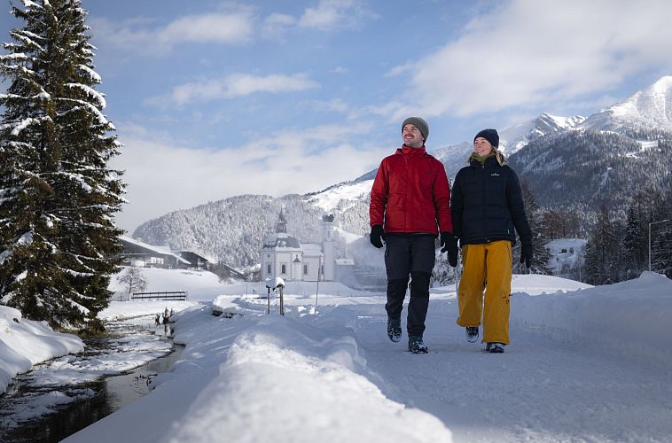 Zwei Personen beim Winterwandern in einer schneebedeckten Landschaft mit Bergen im Hintergrund.