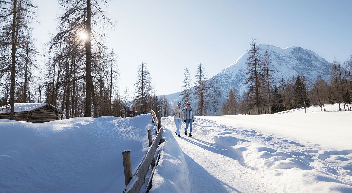 Winterwanderer auf einem schneebedeckten Weg mit Bergen im Hintergrund.