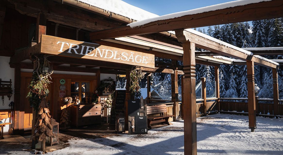 Fassade eines Gebäudes mit dem Schriftzug 'Triendlsage' in einer verschneiten Umgebung.