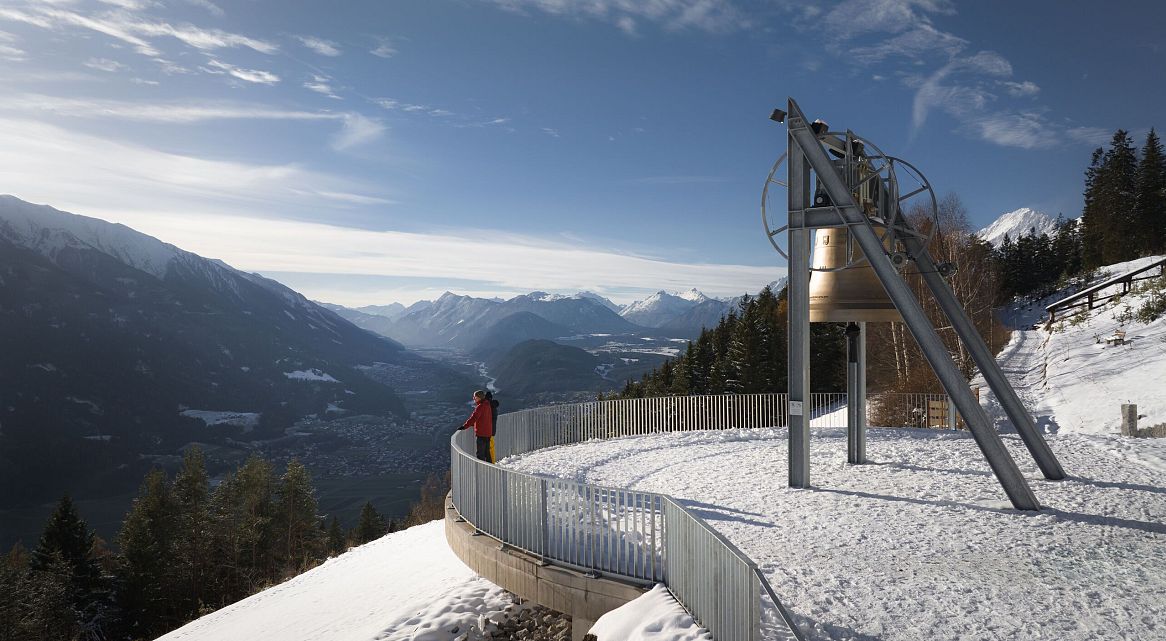 Person in roter Kleidung auf Aussichtsplattform mit Blick auf schneebedeckte Berge.