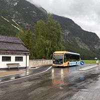 Ein Bus fährt auf einer nassen Straße mit Bergen im Hintergrund.