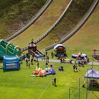 Eine Wiese mit mehreren Hüpfburgen, Spielständen und Menschen, die an einem Freizeitevent teilnehmen.