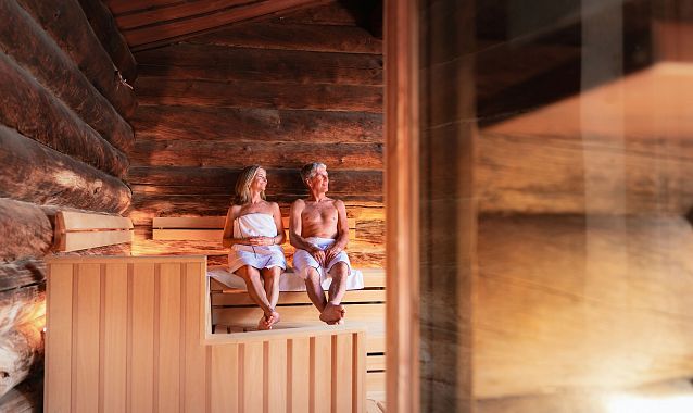 Zwei Personen entspannen in einer Sauna aus Holz in der Region Seefeld, umgeben von warmem Licht und Holzverkleidung.
