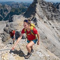 Zwei Bergsteiger auf einem steilen Grat in den Alpen, die Frau vorne lächelt.