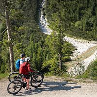 E-Biken im Gaistal im Sommer_zwei Biker_innen auf Forstweg blicken hinab auf Ache