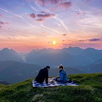 Ein Paar sitzt beim Sundowner Picknick mit Blick Richtung Leutasch