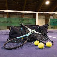 Tennisschläger und Tennisbälle auf einem Hallenplatz in der Region Seefeld vor einem Netz.