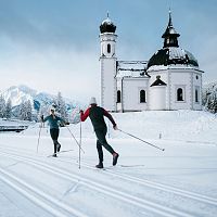 Langläufer vor verschneiter Kapelle in der Region Seefeld, umgeben von Bergen.