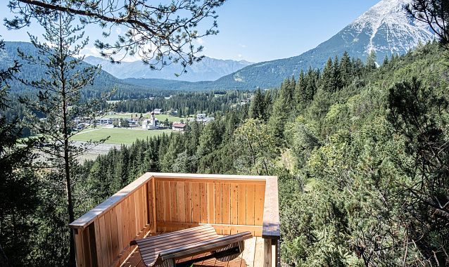 Wooden viewpoint overlooking a green valley and mountains under a blue sky.