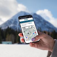 Hand hält Smartphone mit Karte der Region Seefeld. Dahinter schneebedeckte Berge und blauer Himmel.