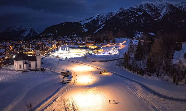 Verschneite Winterlandschaft in der Region Seefeld bei Nacht, beleuchtete Kapelle, umliegende Berge.