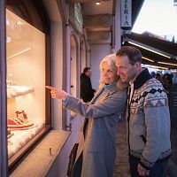 Ein älteres Paar betrachtet gemeinsam ein festlich dekoriertes Schaufenster in einer belebten Straße.