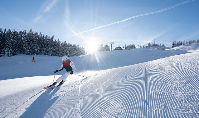 Skifahrer auf sonniger, schneebedeckter Piste in der Region Seefeld. Perfekt präparierte Spuren leuchten im Sonnenlicht.