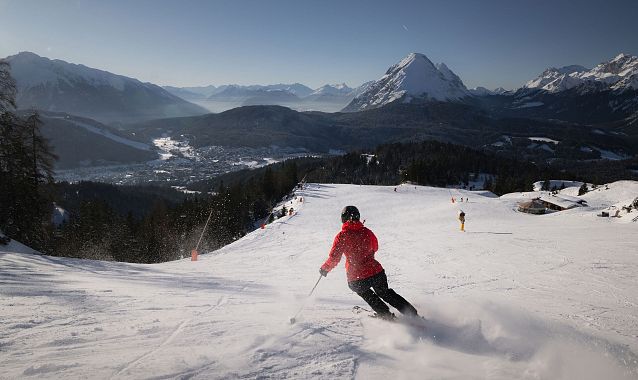 Skifahrer fährt Piste in der Region Seefeld hinunter, Alpen im Hintergrund.
