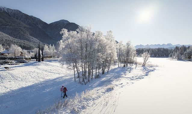 Winterwandern in der Region Seefeld_Drohnenaufnahme_Mann und Frau laufen entlang des Ufers des Wildsees