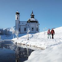 Verschneite Kirche in Winterlandschaft, Wanderer im Vordergrund. Region Seefeld. Klarer Himmel, blau.