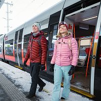 Winterwandern in der Region Seefeld_Mann und Frau steigen aus dem Zug in Seefeld aus_Frau blickt nach oben