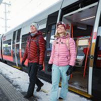 Winterwandern in der Region Seefeld_Mann und Frau steigen aus dem Zug in Seefeld aus_Frau blickt nach oben